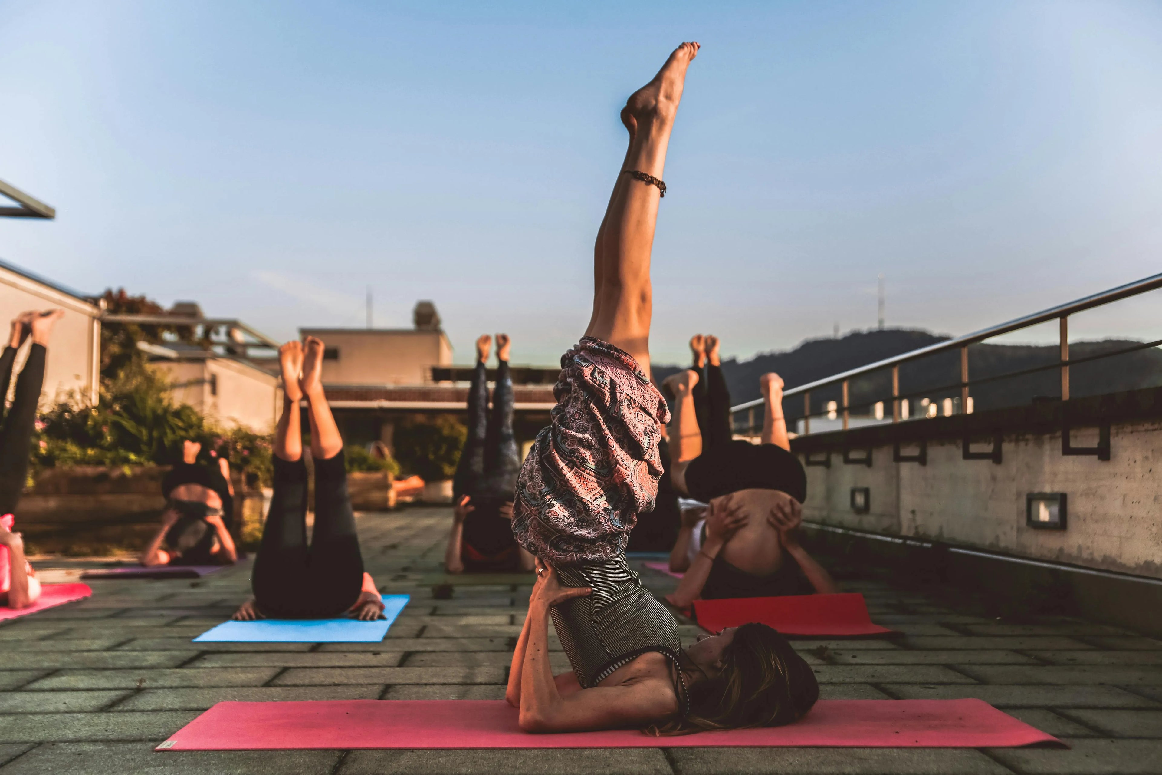 A group of people practicing shoulder stand pose on yoga mats outdoors at sunset, enhancing flexibility and balance.