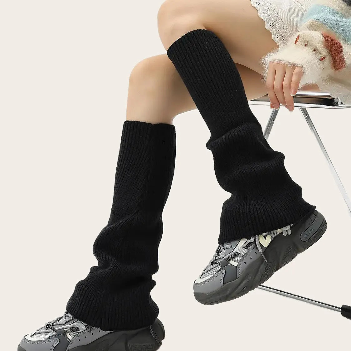 Black ribbed knit over-the-knee leg warmers for women styled with winter sneakers.