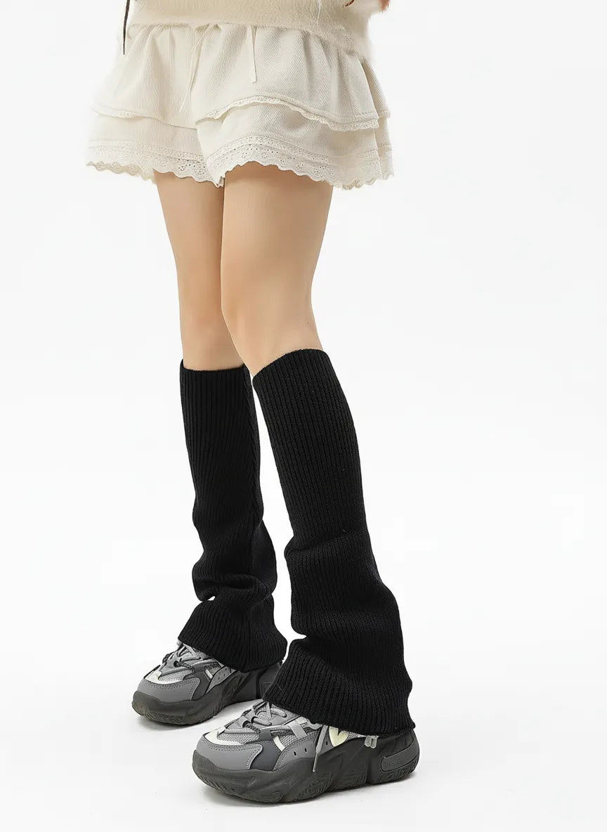 Black ribbed knit leg warmers paired with chunky sneakers and a lace-trim skirt; slouchy mid-calf fit for fall/winter layering.
