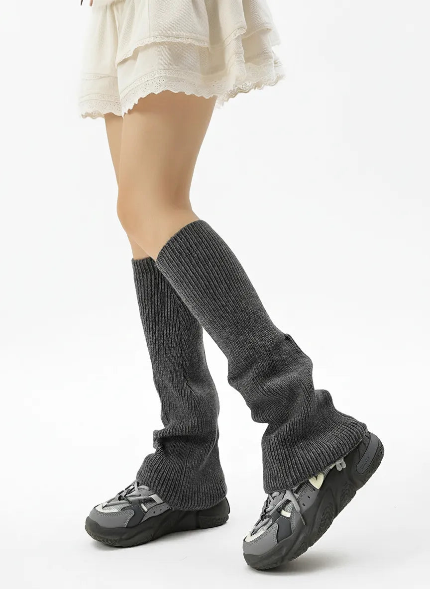 Charcoal grey knit leg warmers with athletic sneakers; slouchy mid-calf coverage for cold weather.
