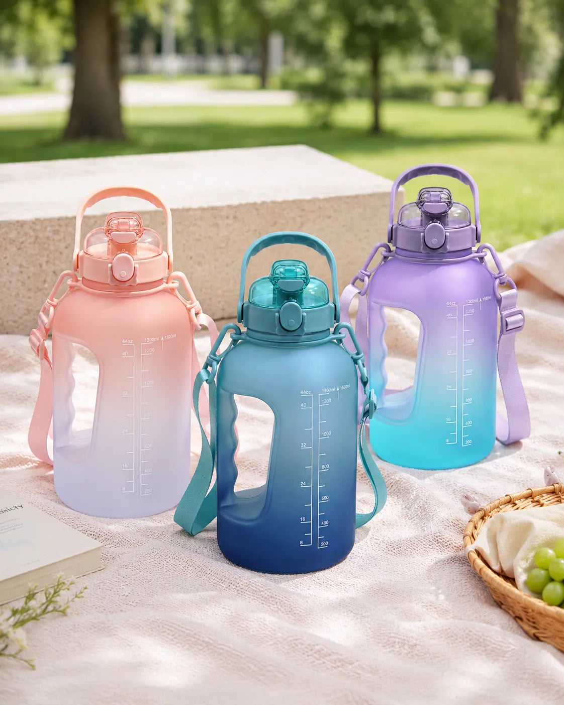 Pink, blue and purple Sportive Lives large sports water bottles with handles and shoulder straps displayed outdoors.