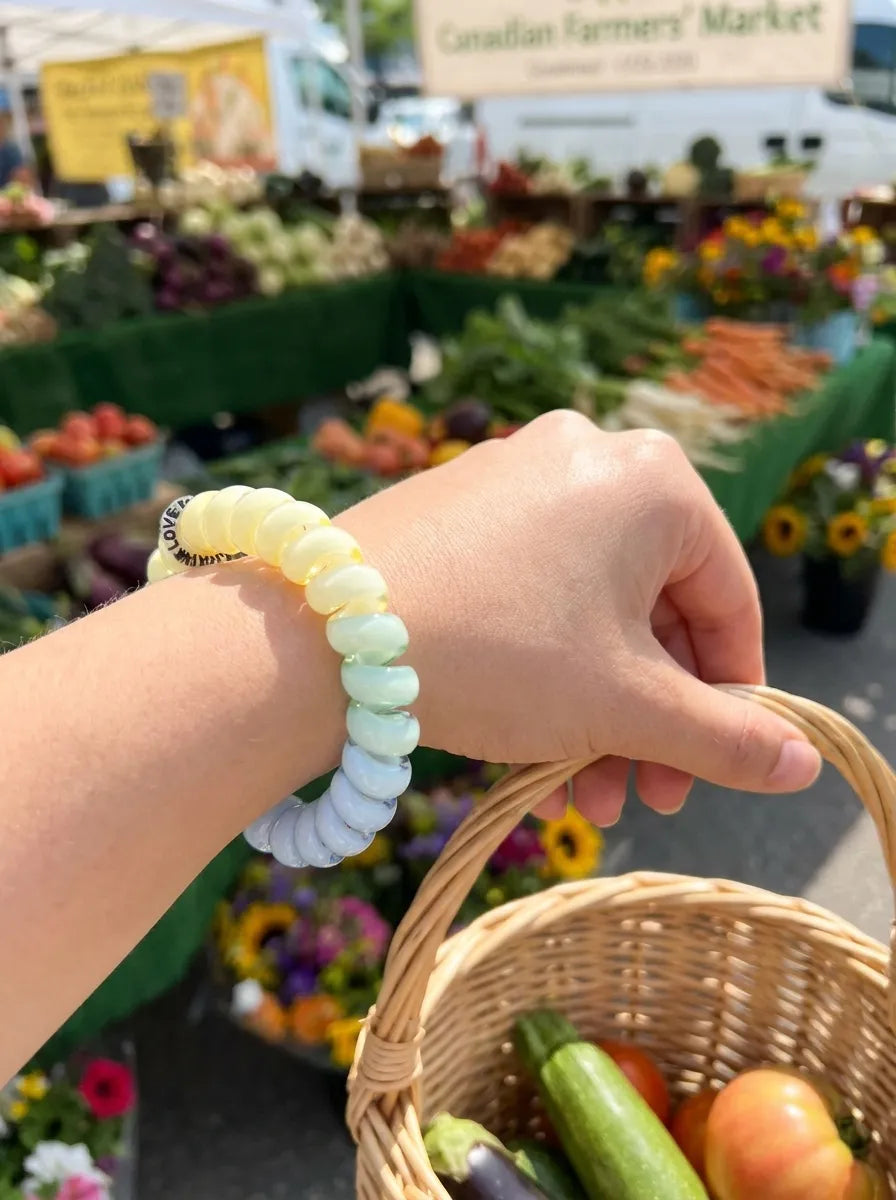 Pastel Jelly Spiral Hair Tie worn on the wrist while carrying a market basket at an outdoor farmers market.