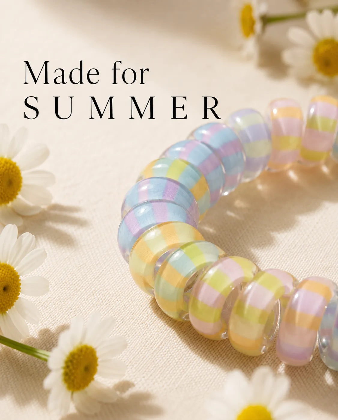 Close-up of a glossy pastel striped Jelly Spiral Hair Tie displayed with summer daisies.