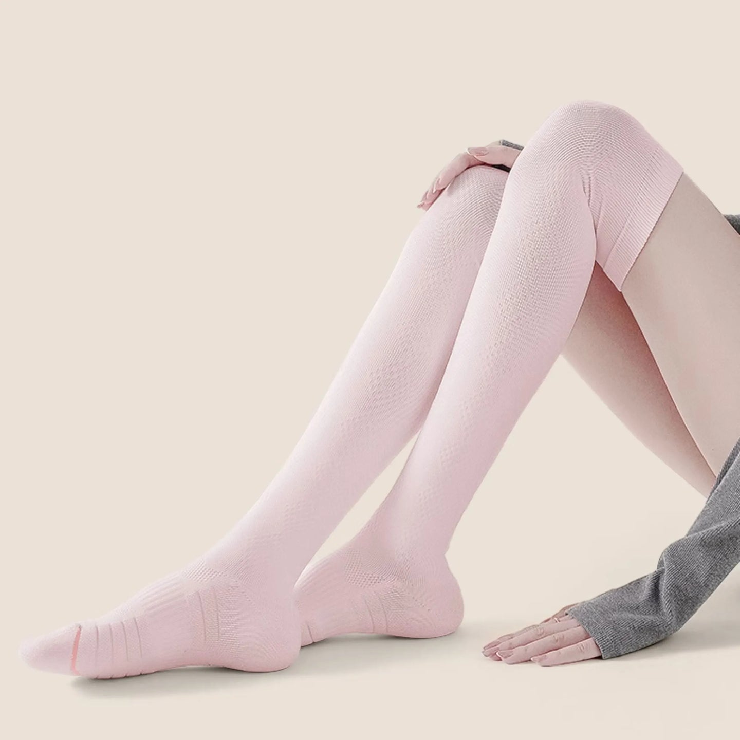 Woman wearing pink over-the-knee compression socks, showcasing slim fit and ergonomic foot support design