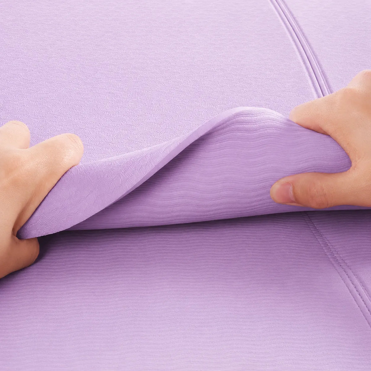 Hands bending a 6 mm purple TPE yoga mat to show its flexible cushioning