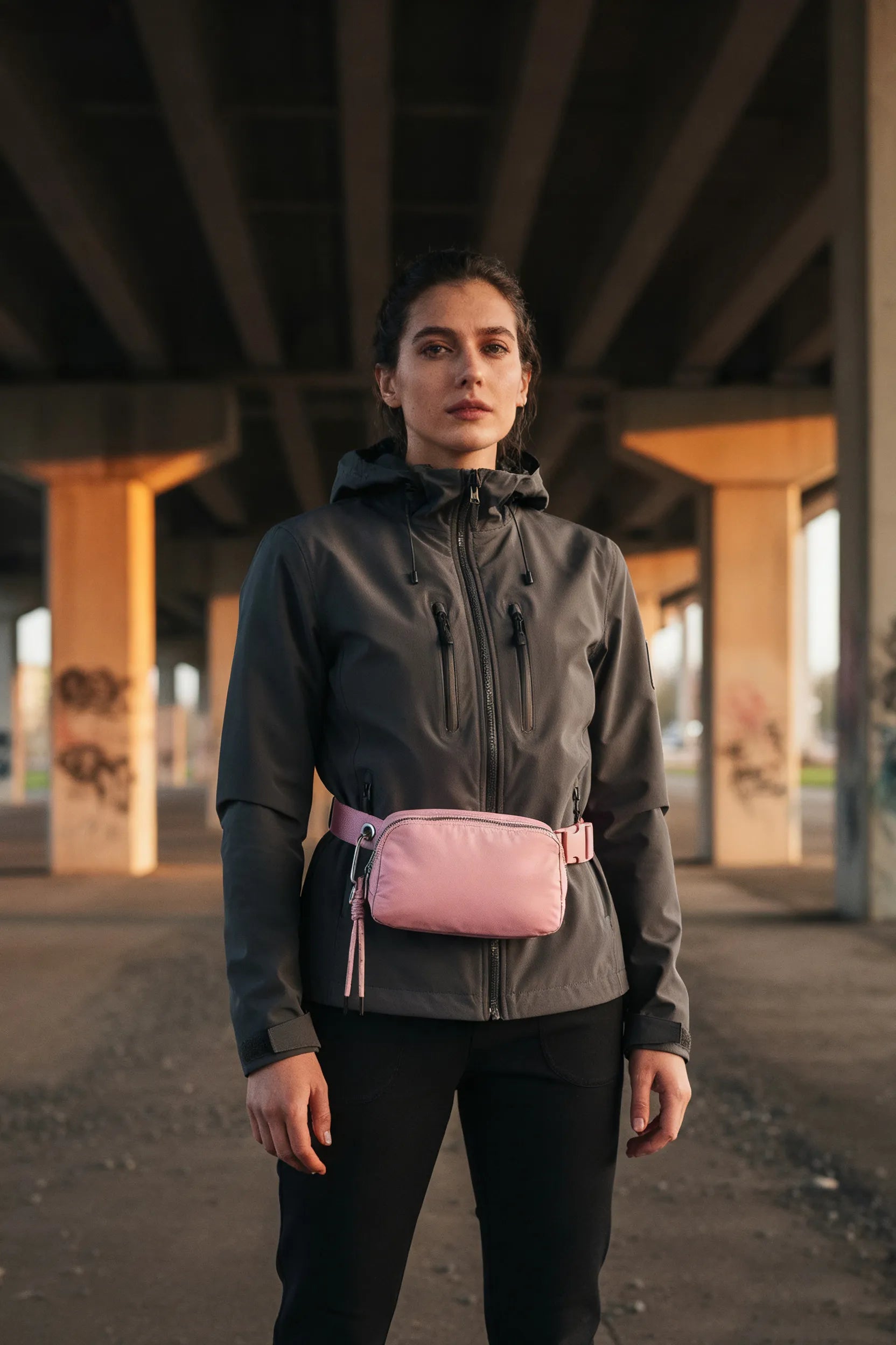 Woman in technical jacket wearing a pink belt bag for outdoor activity.