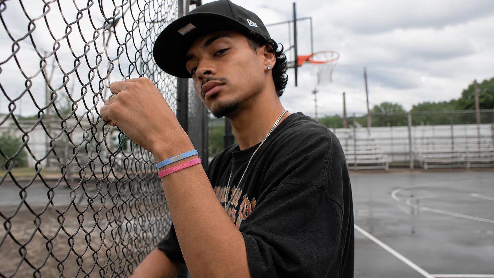 Man wearing blue FAITH and pink COURAGE silicone wristbands by an outdoor basketball court