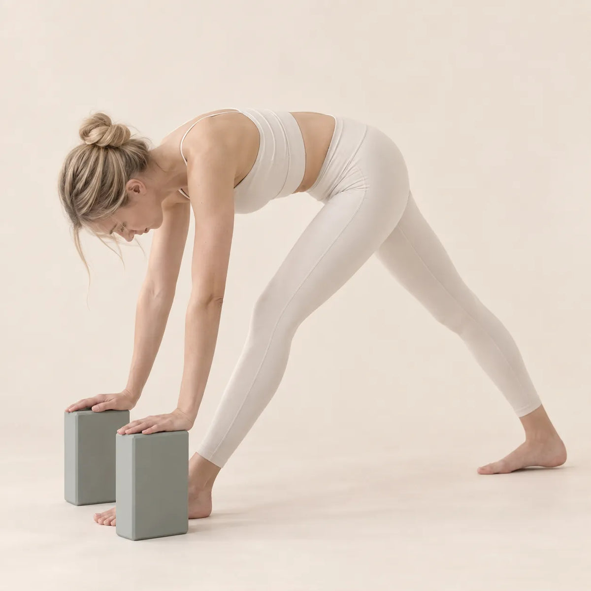 Woman using two grey EVA yoga blocks for hand support during a standing forward fold stretch.