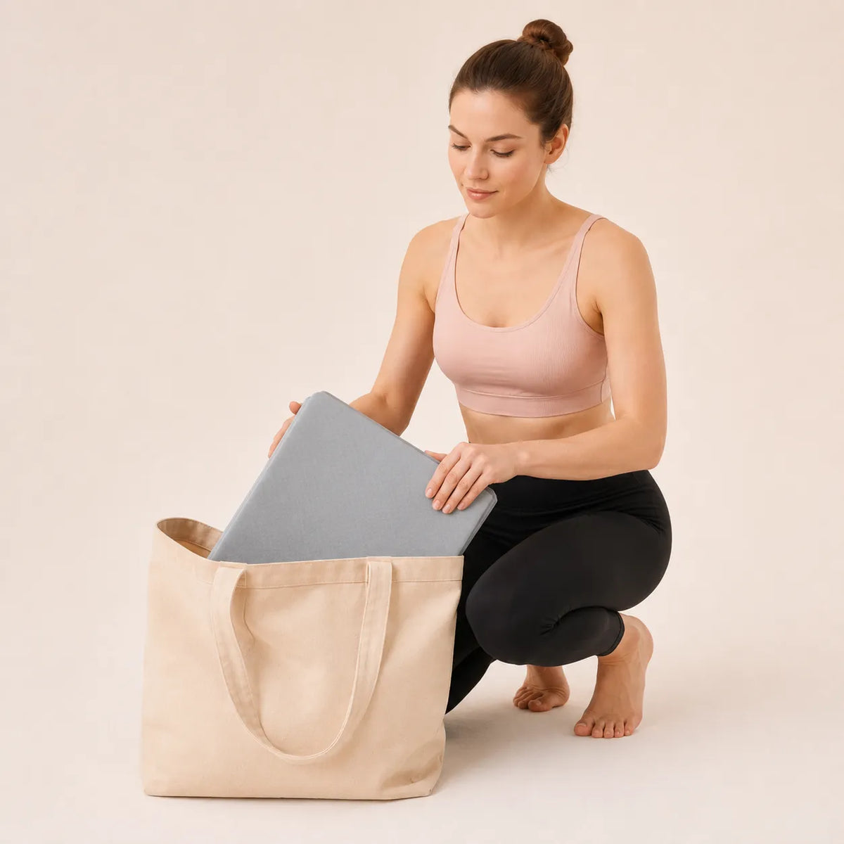 Woman packing a grey foldable yoga mat into a tote bag for easy storage and travel.