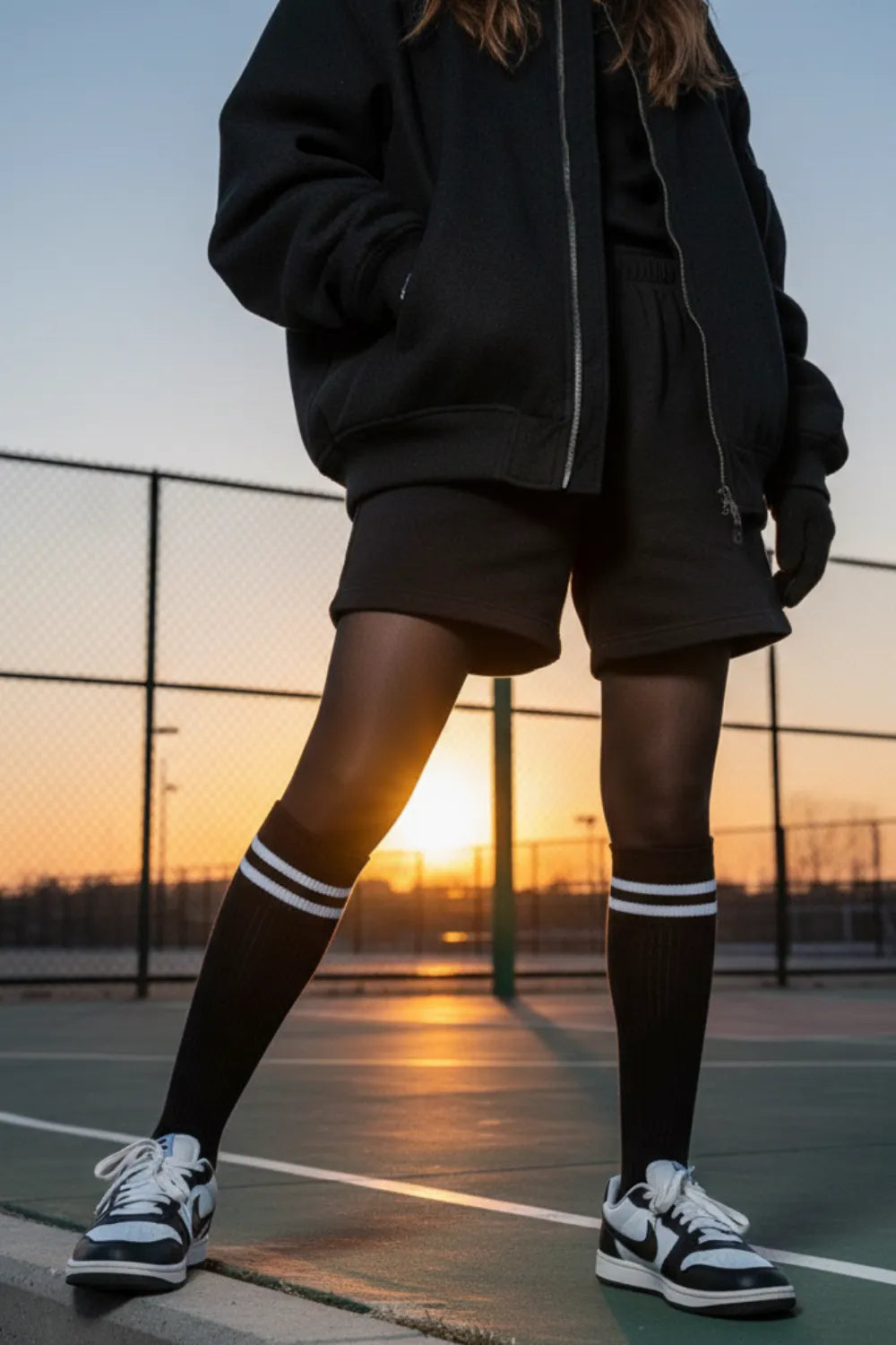 Black knee-high striped socks styled with sneakers on a sport court at sunset.