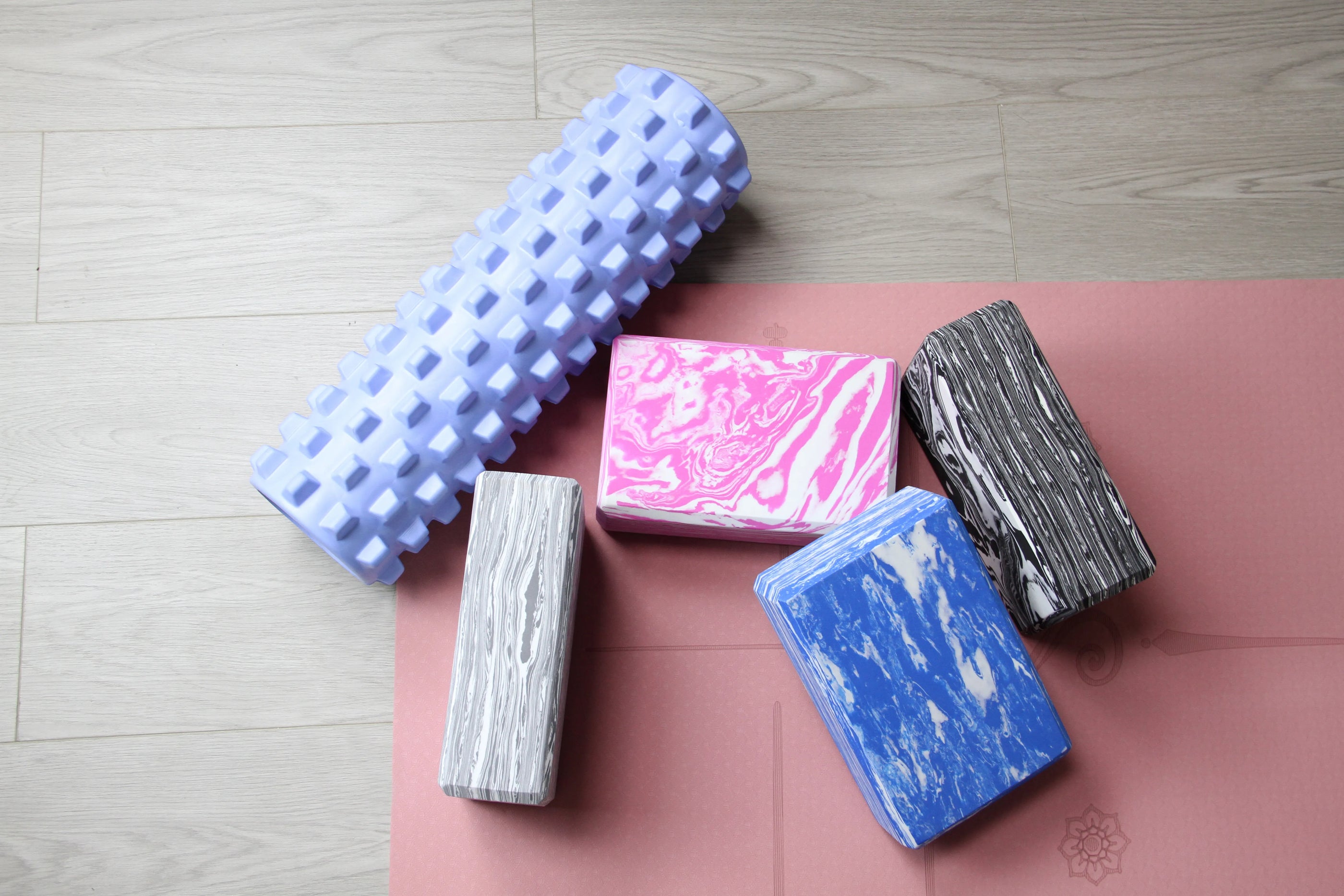 Sportive Lives yoga blocks (gray, pink, black, blue) and ice blue EVA massage roller used on yoga mat for muscle recovery and pose support, perfect for yoga practice in Canada.