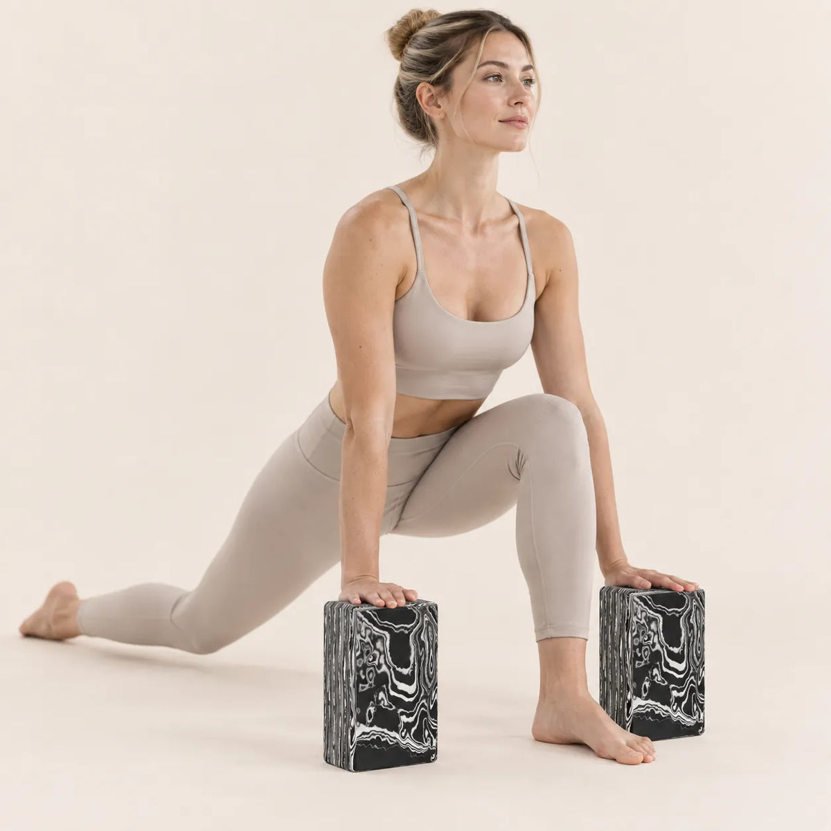 Woman using two marbled yoga blocks for hand support during a low lunge stretch.
