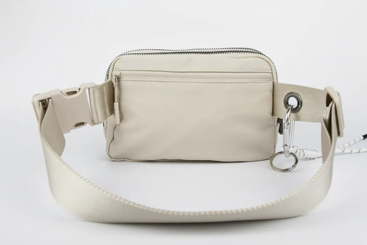 Back view of beige waterproof nylon belt bag with exterior zip security pocket, adjustable strap and metal carabiner ring.